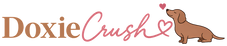 A graphic logo featuring the text 'Doxie Crush' with a pink heart and a brown cartoon dachshund on a white background.