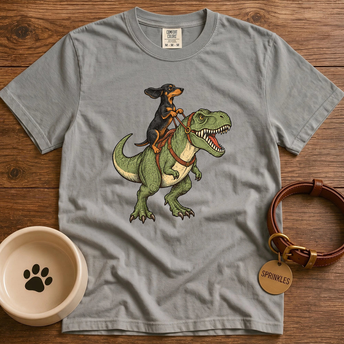 Grey Vintage-style illustration of a red dachshund riding a green T-Rex dinosaur, holding leather reins, with windblown ears and detailed hand-drawn artwork.