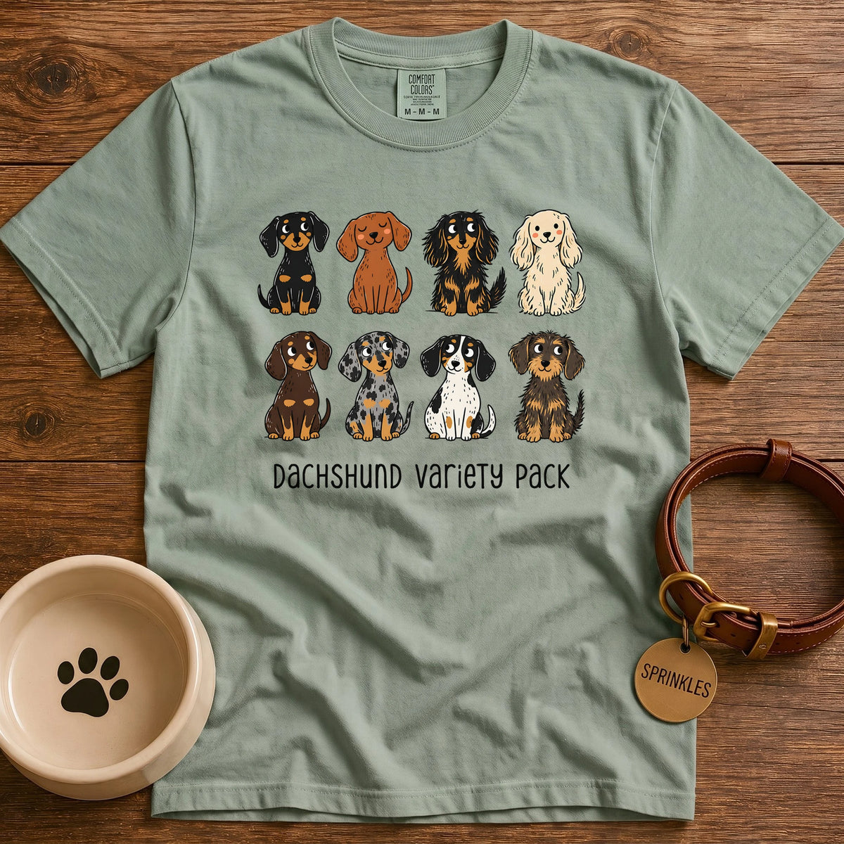 Bay Green Comfort Colors t-shirt with a “Dachshund Variety Pack” graphic of eight cartoon dachshunds in different coats and colors, including black and tan, red, cream, chocolate, dapple, piebald, longhaired, and wirehaired.
