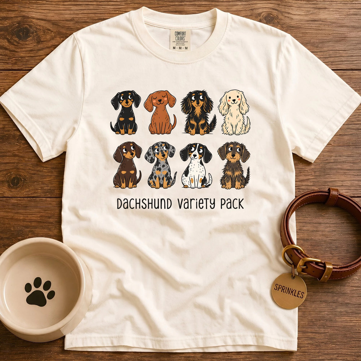 Ivory Comfort Colors t-shirt with a “Dachshund Variety Pack” graphic of eight cartoon dachshunds in different coats and colors, including black and tan, red, cream, chocolate, dapple, piebald, longhaired, and wirehaired.